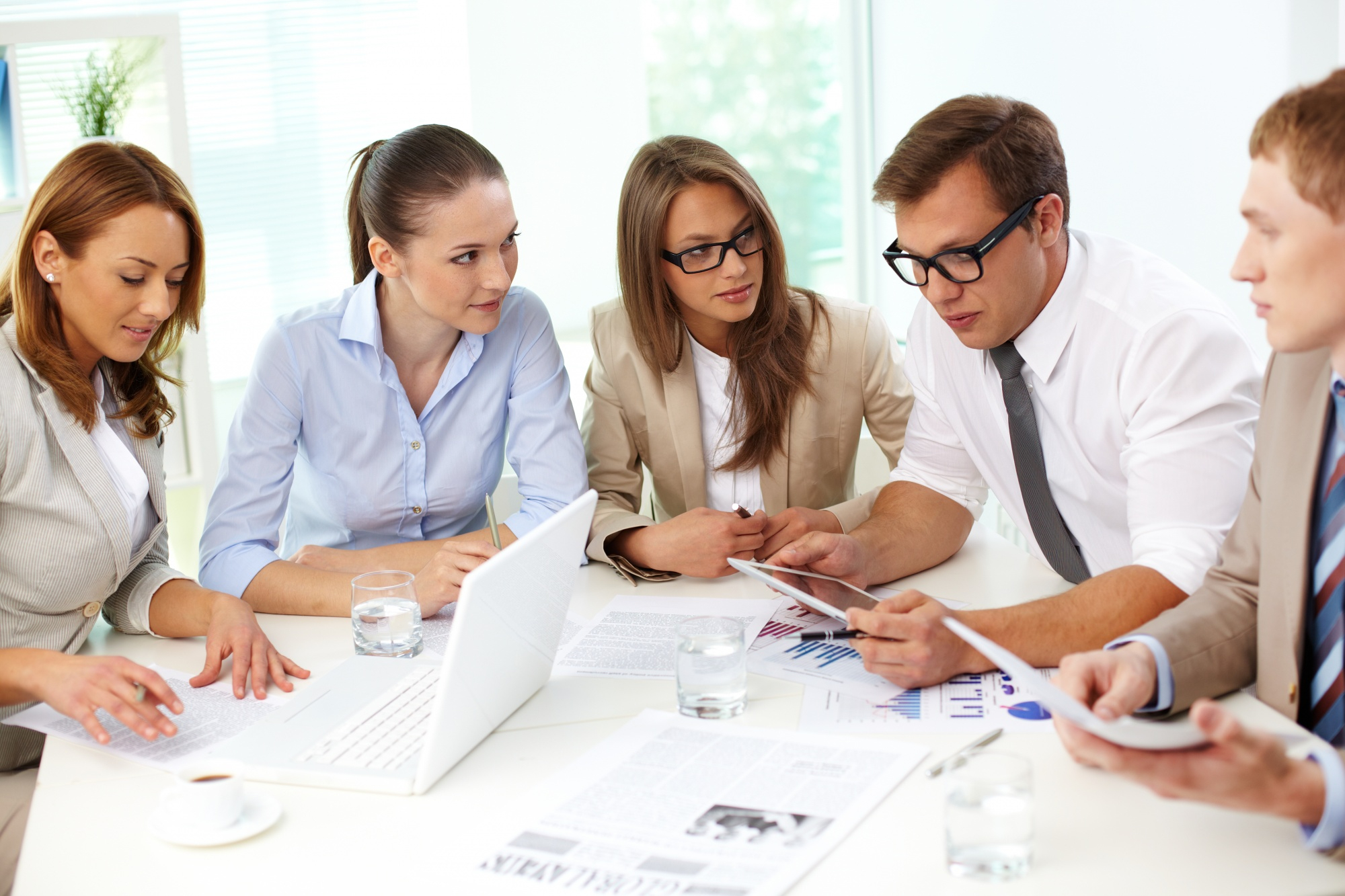 The image should depict a professional and inviting office environment representing accounting services. The scene should include individuals engaging in a business meeting, surrounded by modern office equipment like laptops and documents, symbolizing efficiency and expertise. The setting should convey a sense of reliability and trust, appropriate for a company offering accounting services in the USA. Key elements include diverse professionals discussing financial matters, emphasizing collaboration and innovation.